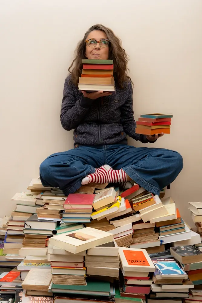 photo d'Elise qui dirige l'agence ipomea correction assise sur une montagne de livre